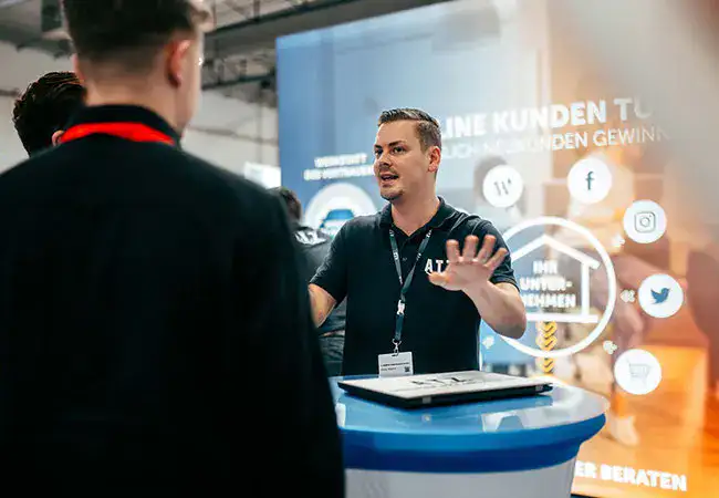 ATZ-Group-Sales-Mitarbeiter unterhält sich am Messestand mit Besuchern